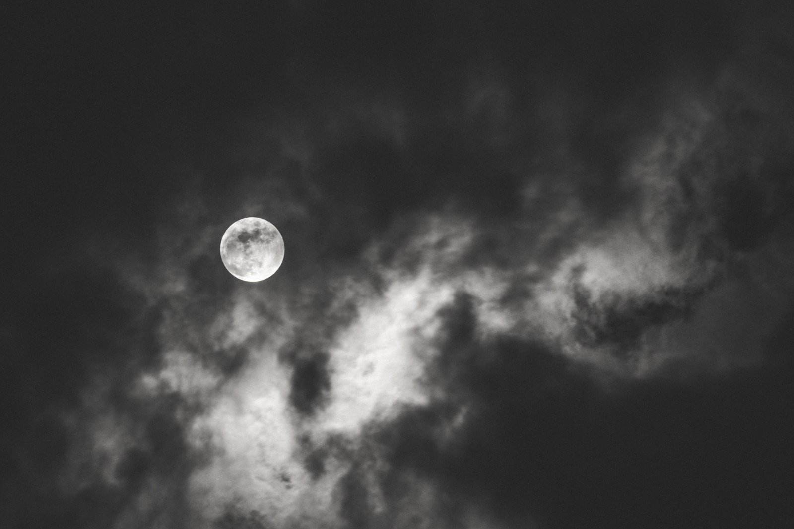 Dark shot of the full moon spreading light behind the clouds during nighttime